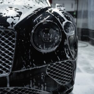 Close-up of a sleek black luxury car with soapy foam during a carwash process.