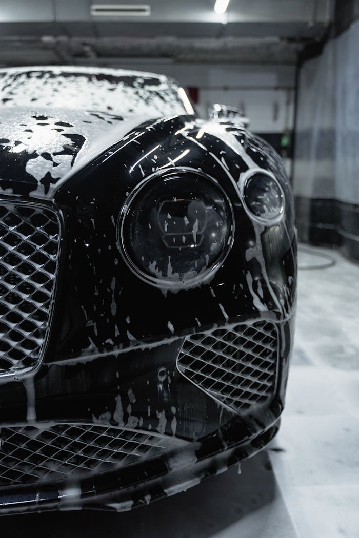 Close-up of a sleek black luxury car with soapy foam during a carwash process.
